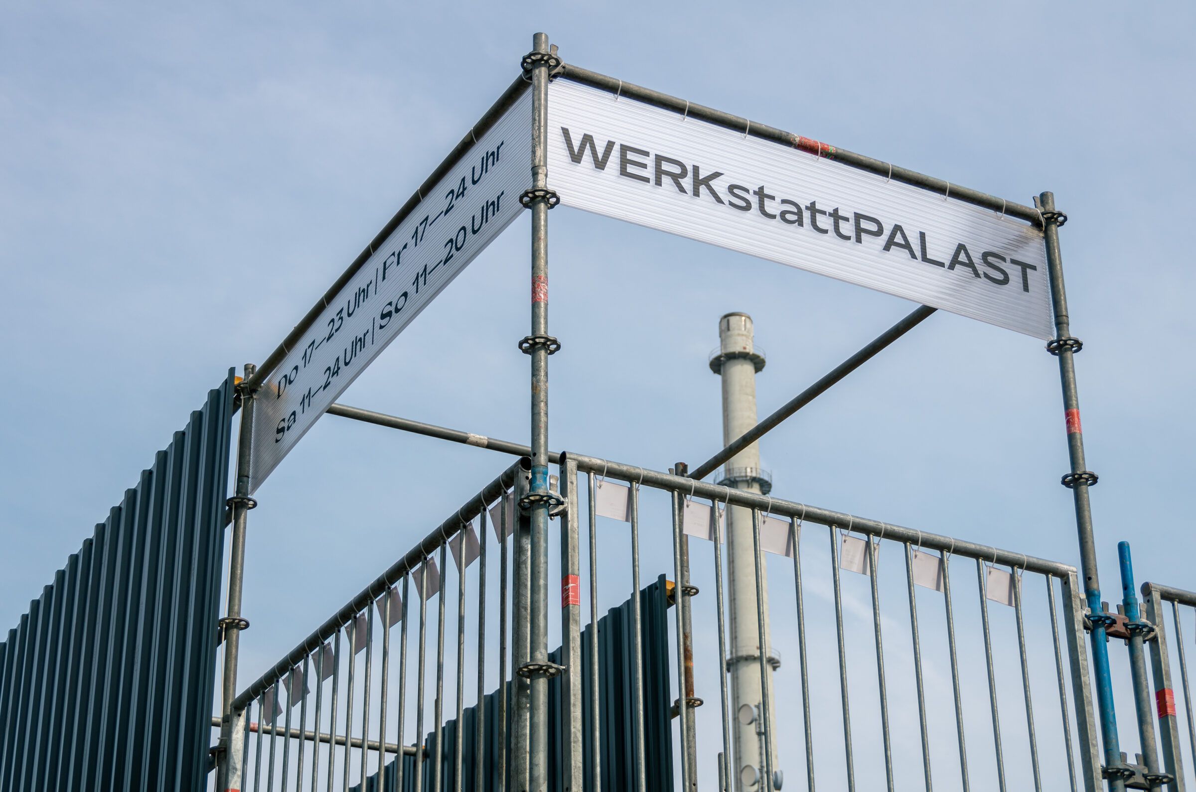 Das Schild mit dem Schriftzug WERKstattPALAST auf dem Gerüst vor blauem Himmel, von unten fotografiert.