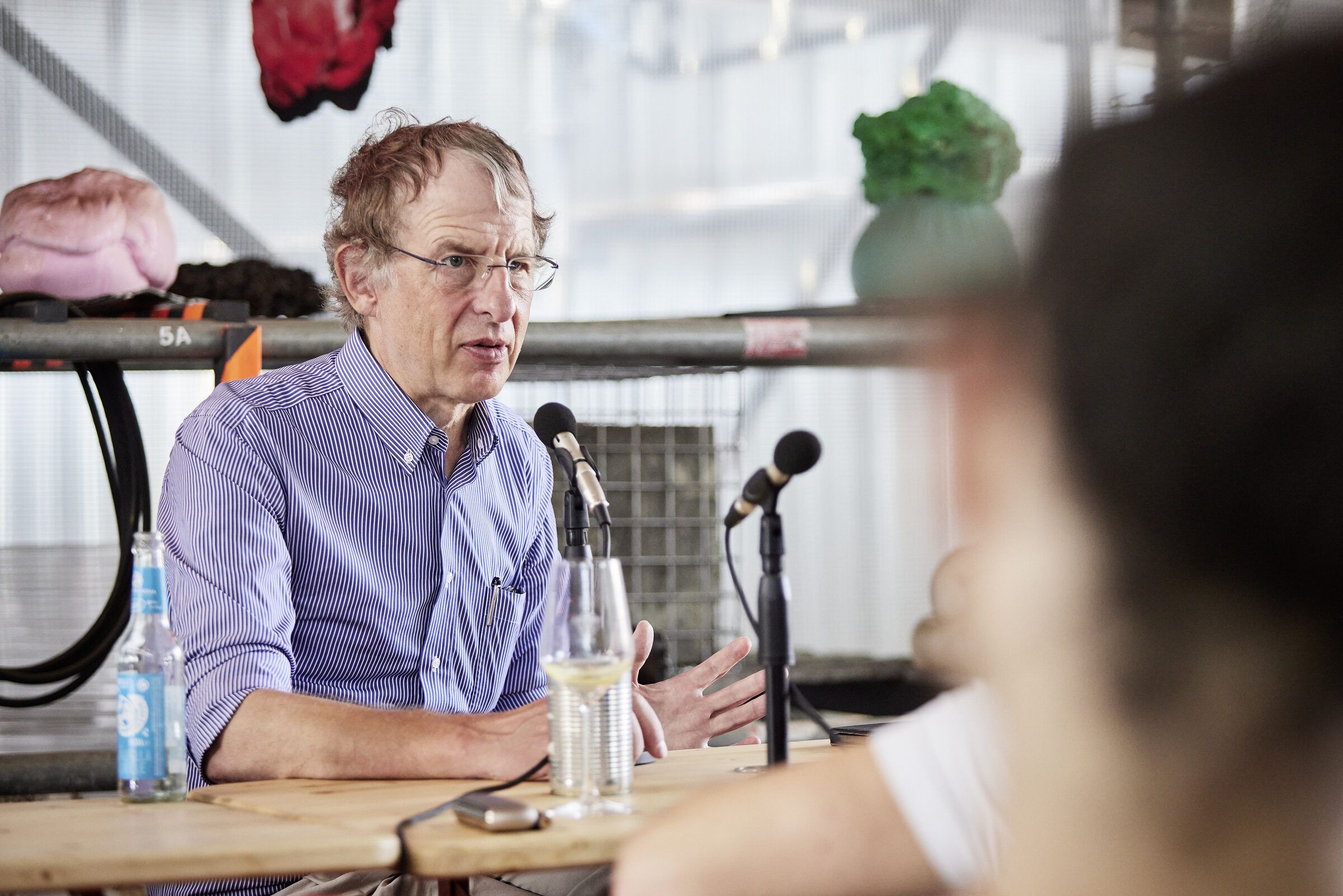 Ein Gesprächsteilnehmer mit Brille spricht an der Tafel in ein Mikrofon.
