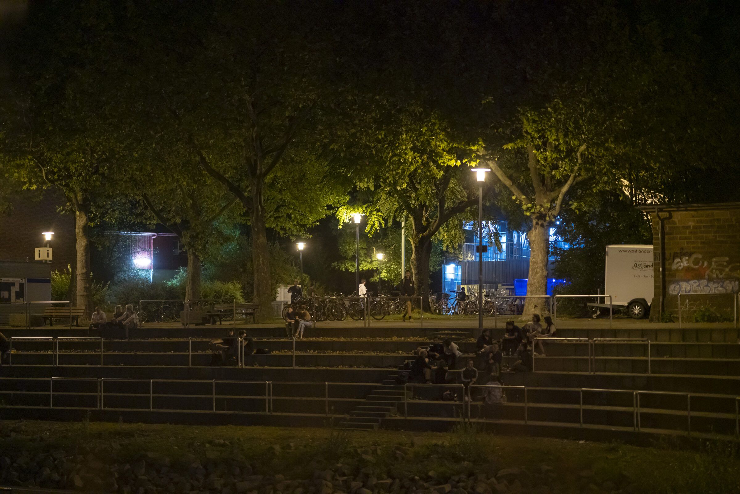 Der nächtliche Park am Hafen mit Stufen, Bäumen und Laternen.