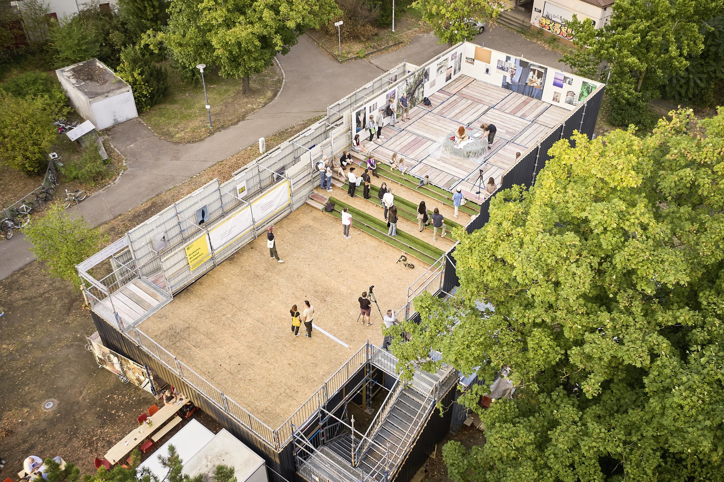 Luftbild von oben auf den Gerüstbau mit Innenhof, Dachterrasse und Treppen, umgeben von Bäumen.