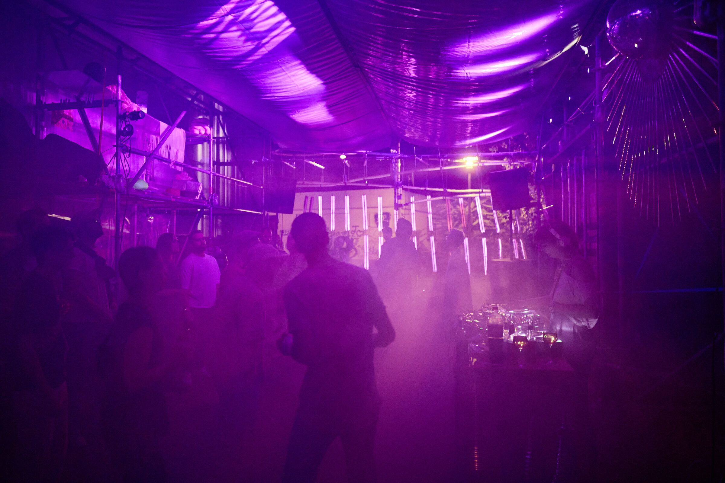 Die Gerüsthalle ist in violettes Licht und Nebel getaucht, Gäste stehen im Gegenlicht.