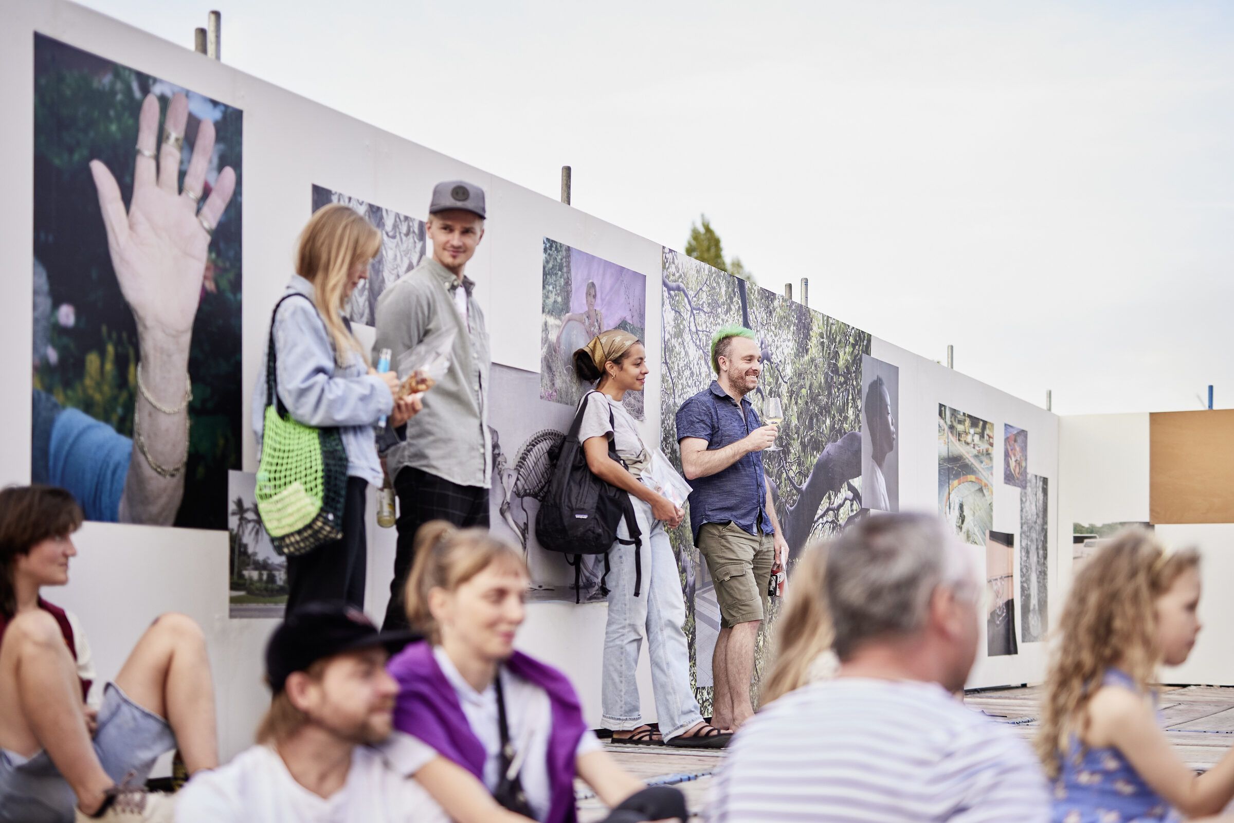 Gäste sitzen und stehen vor der Ausstellungswand mit großformatigen Fotografien.