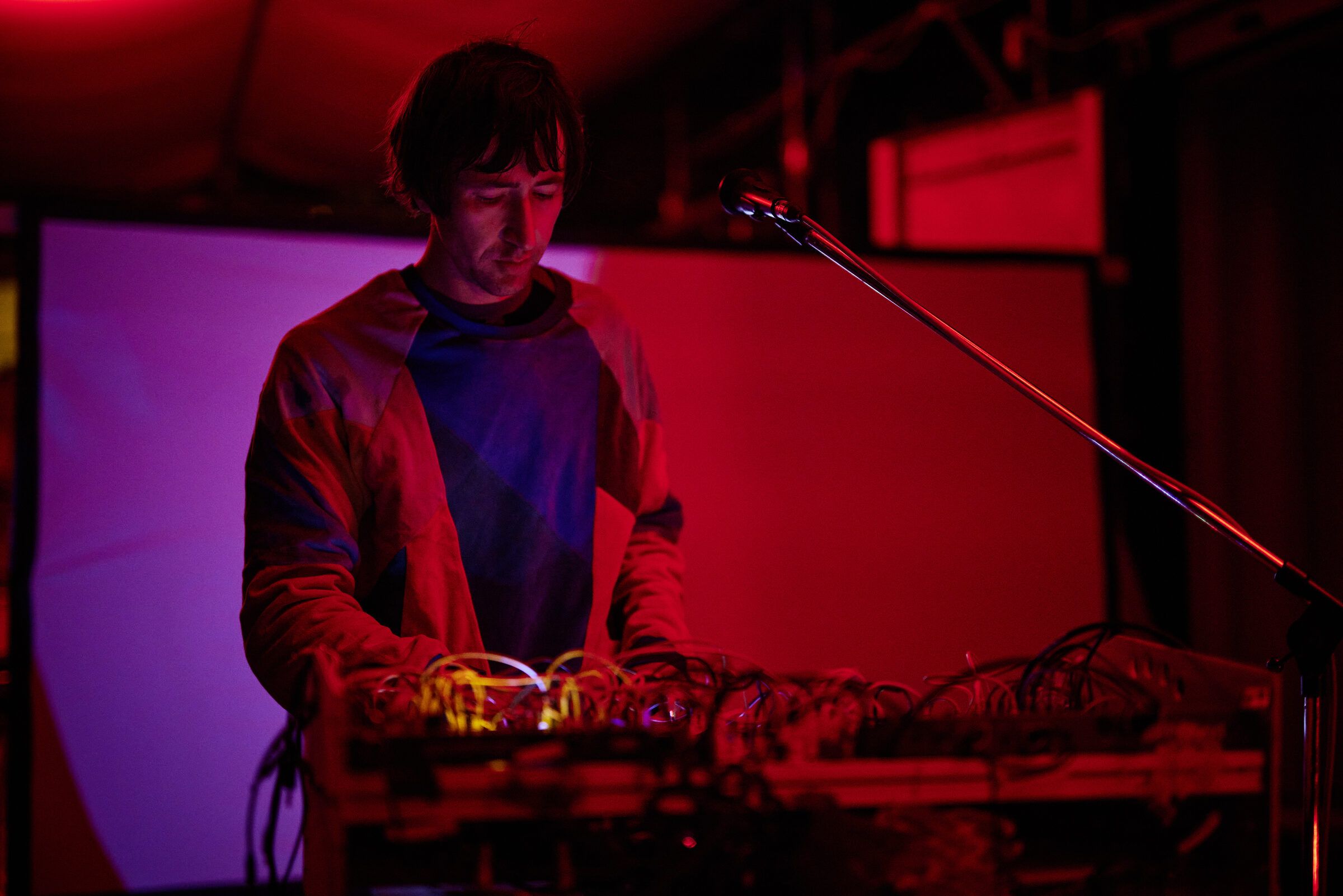 Ein Musiker spielt im roten Licht an einem Tisch mit Synthesizern.