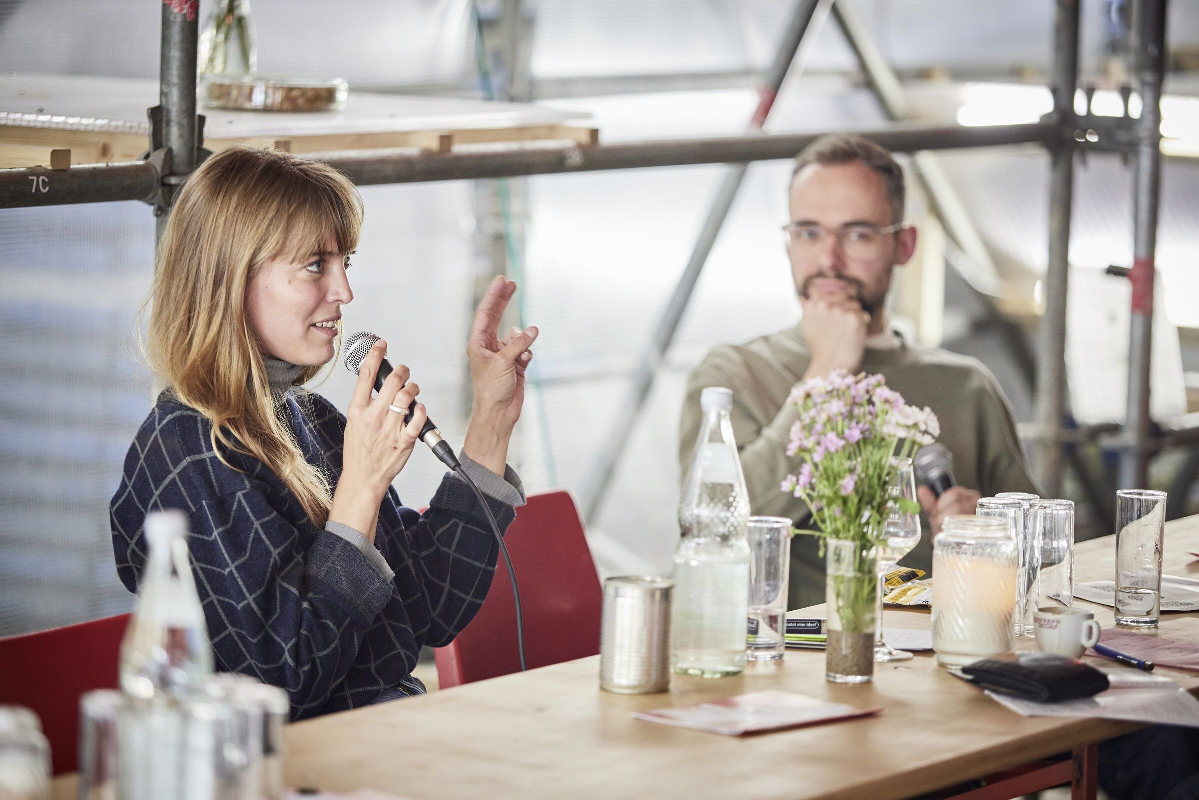 Eine Gesprächsteilnehmerin spricht an der Tafel ins Mikrofon, neben ihr hört ein Mann zu.