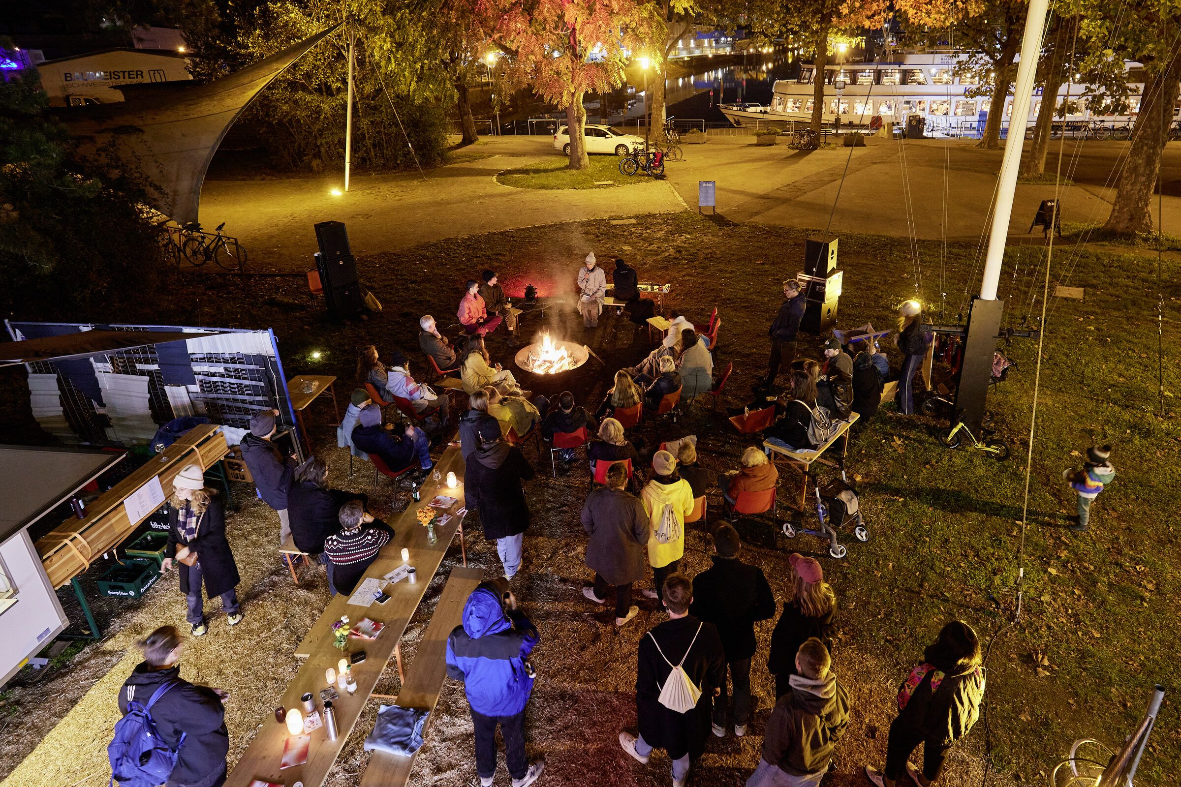 Viele Besuchende versammeln sich nachts im Park am Hafen um mehrere Feuer.