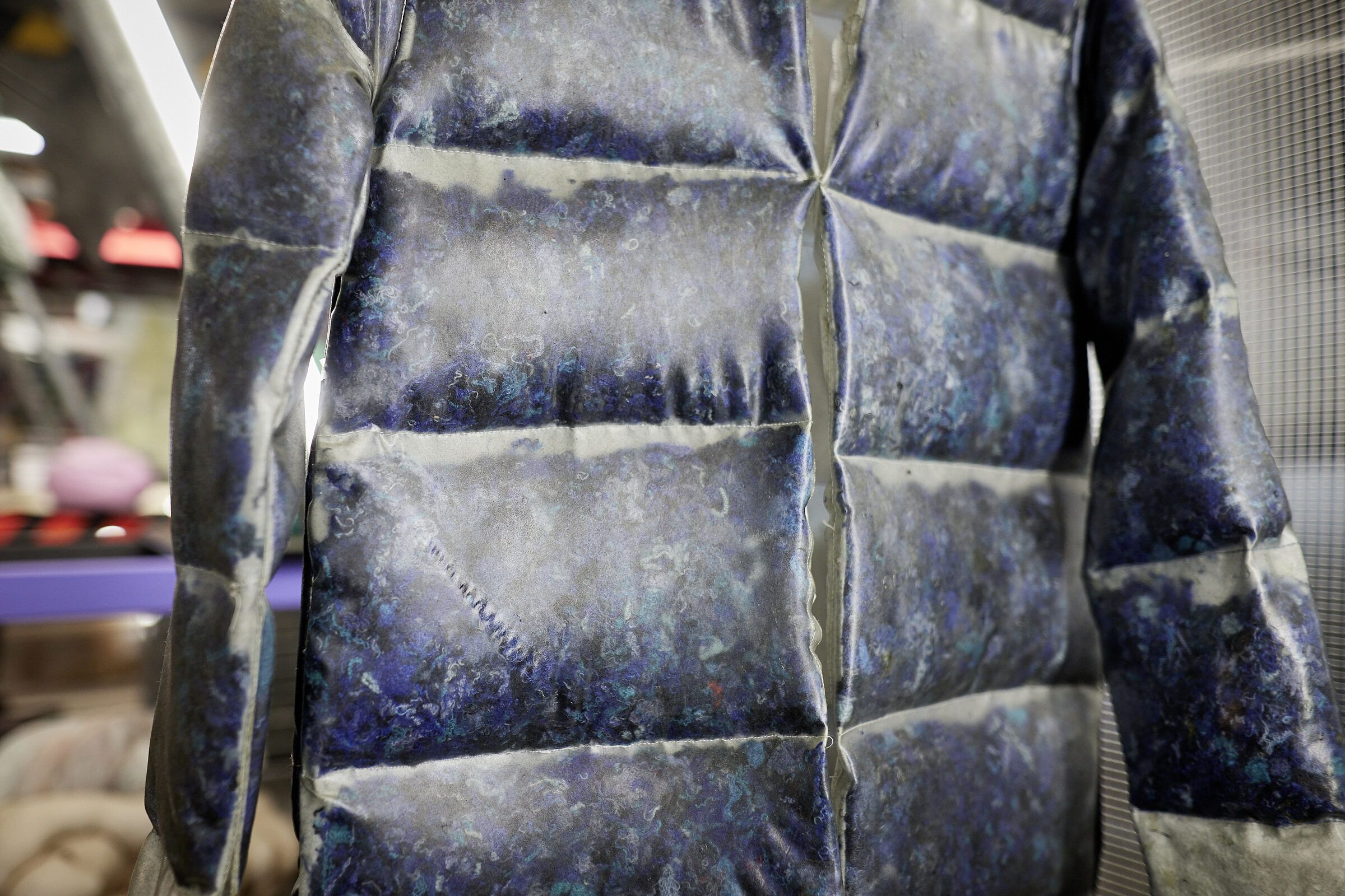 Eine glänzende, dunkelblaue Daunenjacke hängt als Objekt in der Ausstellung.
