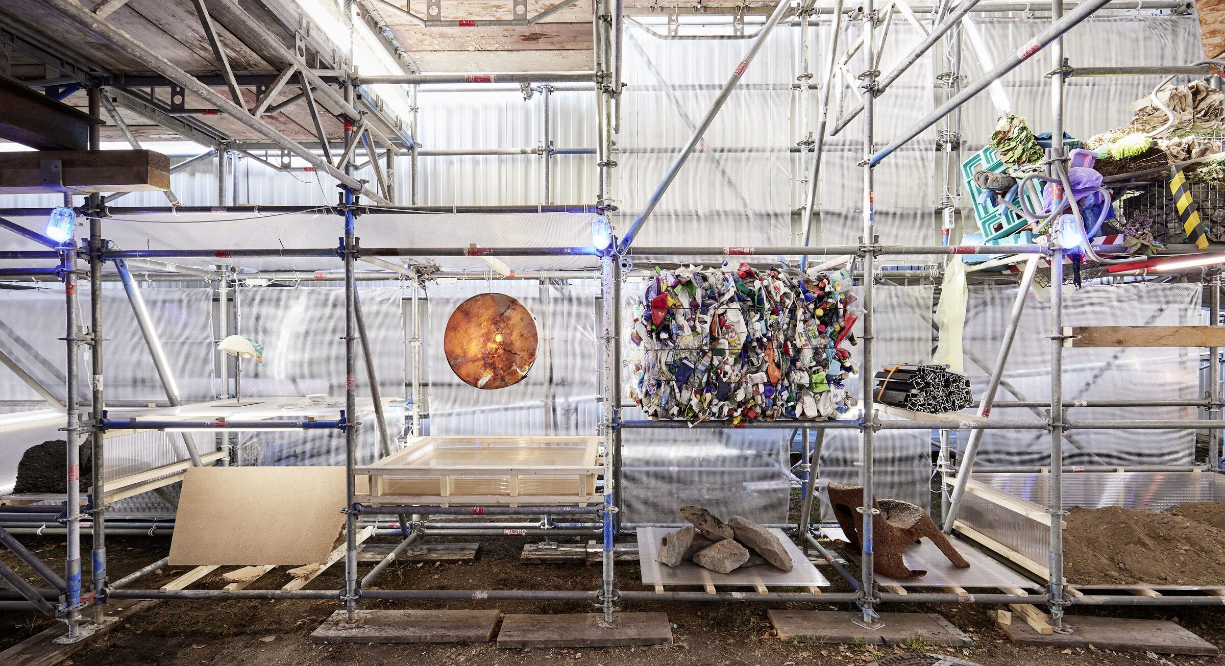 Gesamtansicht des Gerüstregals der Materialbibliothek mit Kunststoffballen, einer orangefarbenen Scheibe und Holzpaletten.
